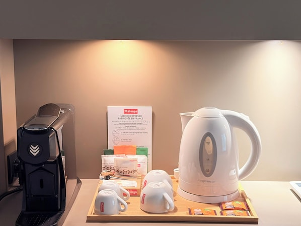 A coffee station with a coffee maker, a kettle, cups, and coffee pods. - Le Prose Hôtel (La Grande-Motte)