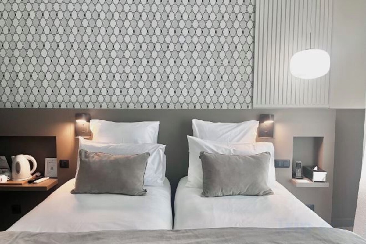 A hotel room with two beds, a patterned wall, and a nightstand with a kettle.