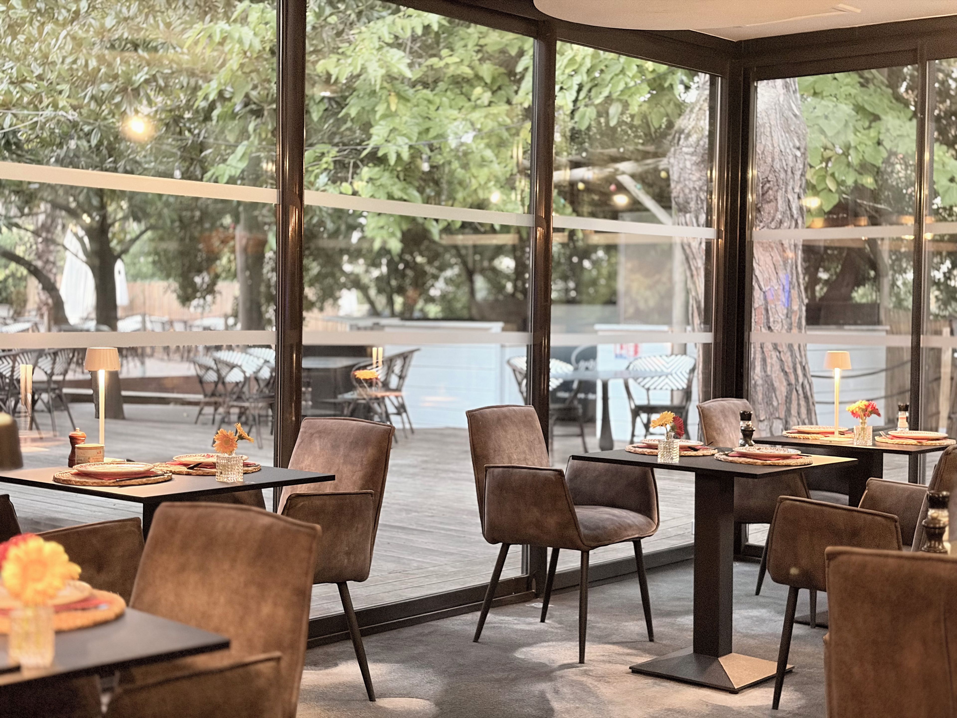 Un comedor interior con mesas y sillas, ventanas amplias y vistas al exterior.