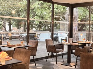 An indoor dining area with tables and chairs, large windows, and a view of the outdoors. - Le Prose Hôtel (La Grande-Motte)