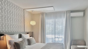 Moderni hotellihuone, jossa on suuri sänky, yöpöytä, tuoli ja näkymä ulos.