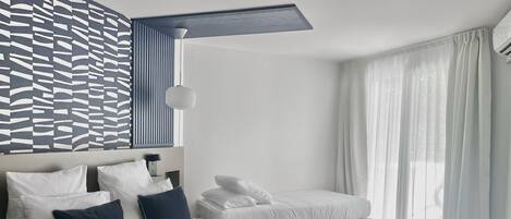 Habitación de hotel moderna con una cama grande, una cama más pequeña y un banco. Pared con diseño y ventana con cortinas traslúcidas.