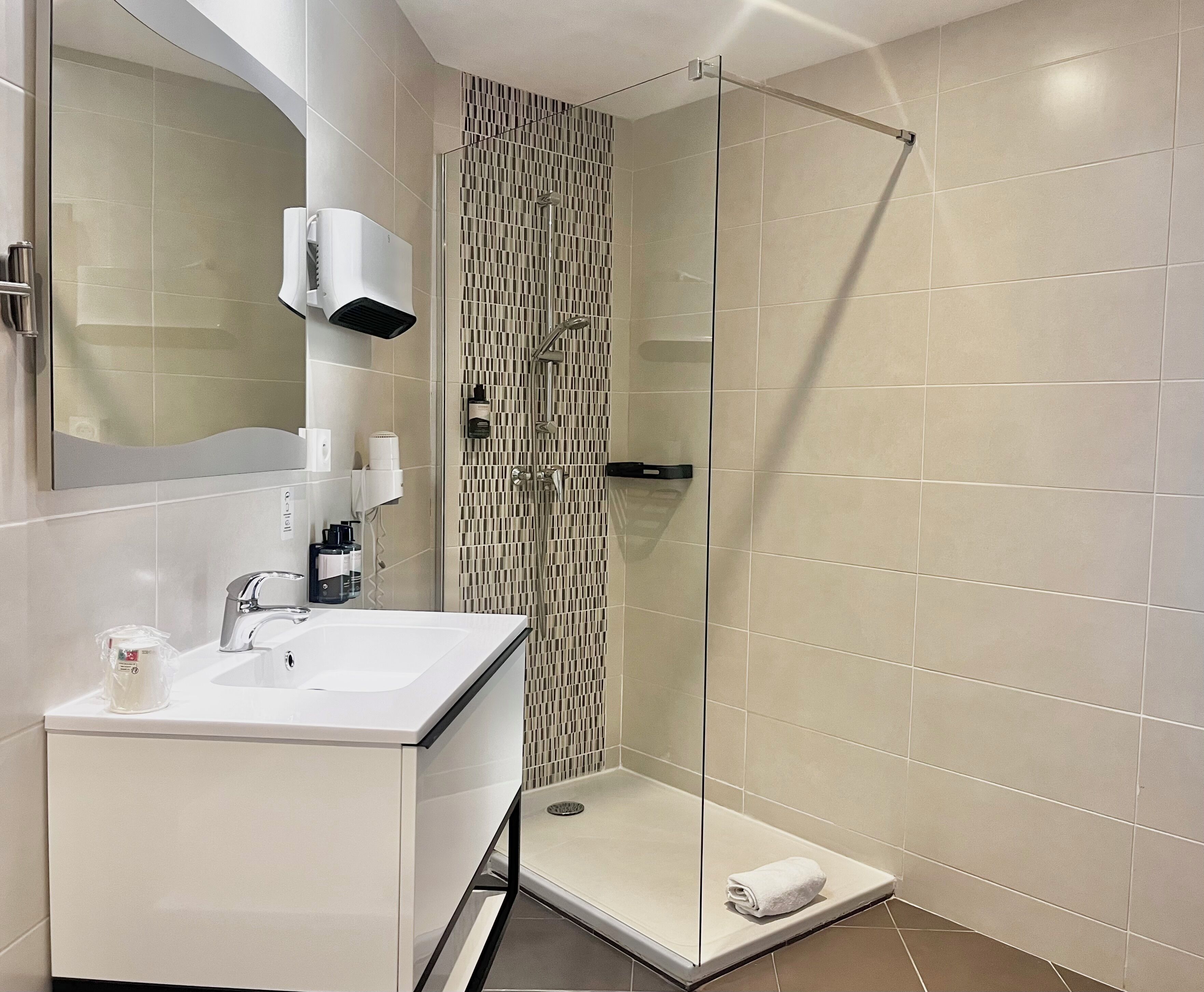 Ein modernes Badezimmer mit einer gläsernen Duschkabine, einem weißen Waschbecken mit Spiegel und einem Handtuch auf dem Boden.