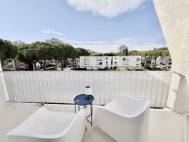 Un balcón con dos sillas blancas y una mesita, con vistas a una zona residencial con árboles y edificios modernos.