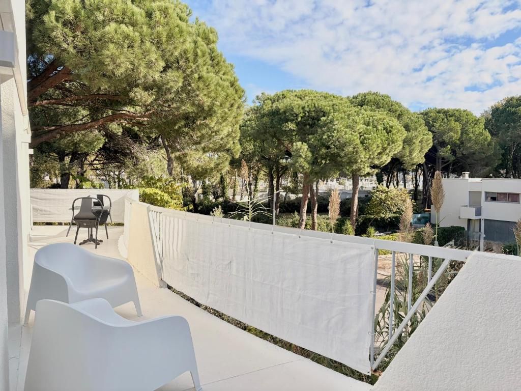 A balcony with white chairs, a white privacy screen, and a view of trees and buildings.
