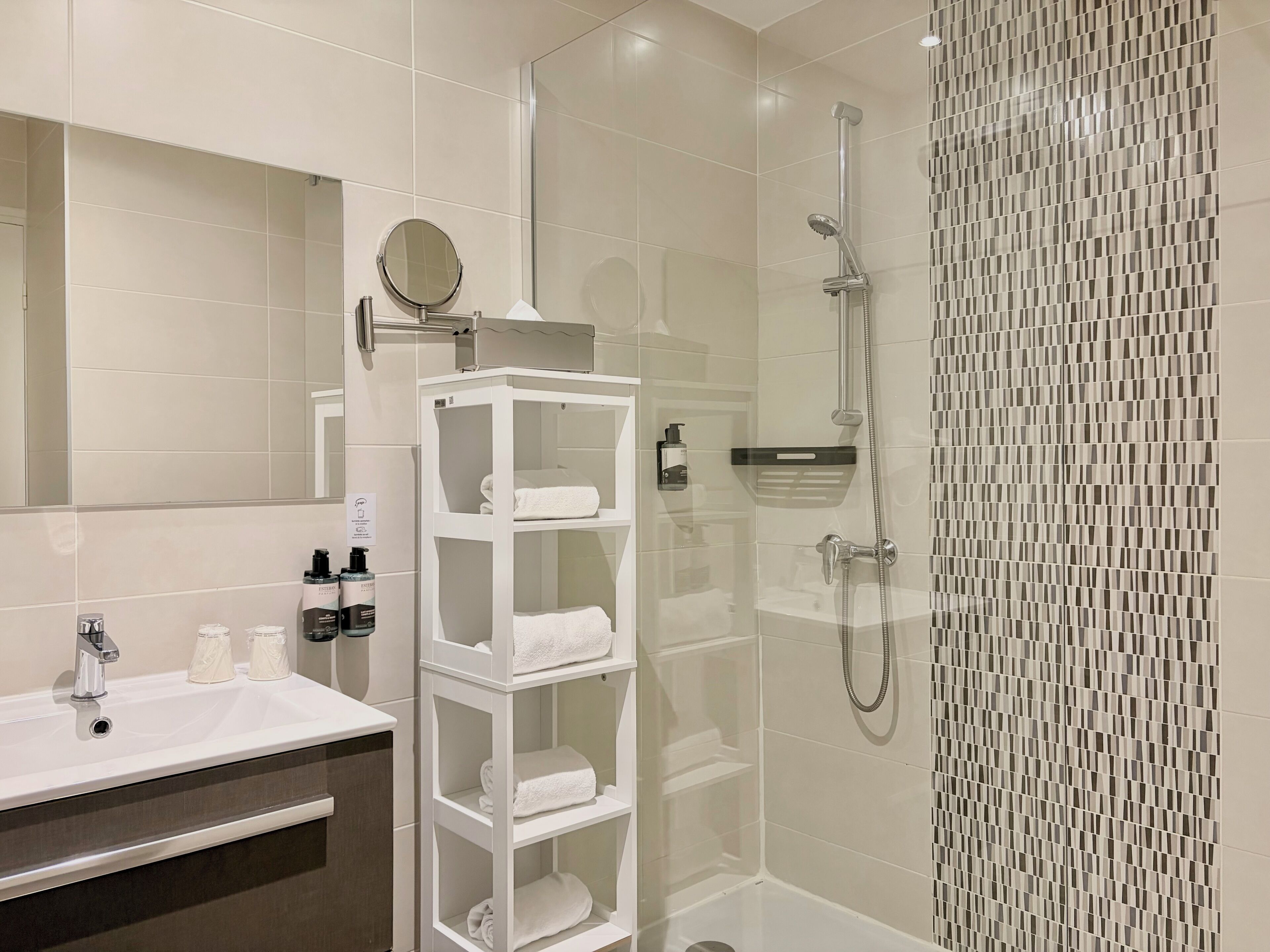 Un baño moderno con ducha envuelta en vidrio, tocador blanco con espejo y repisa con toallas.