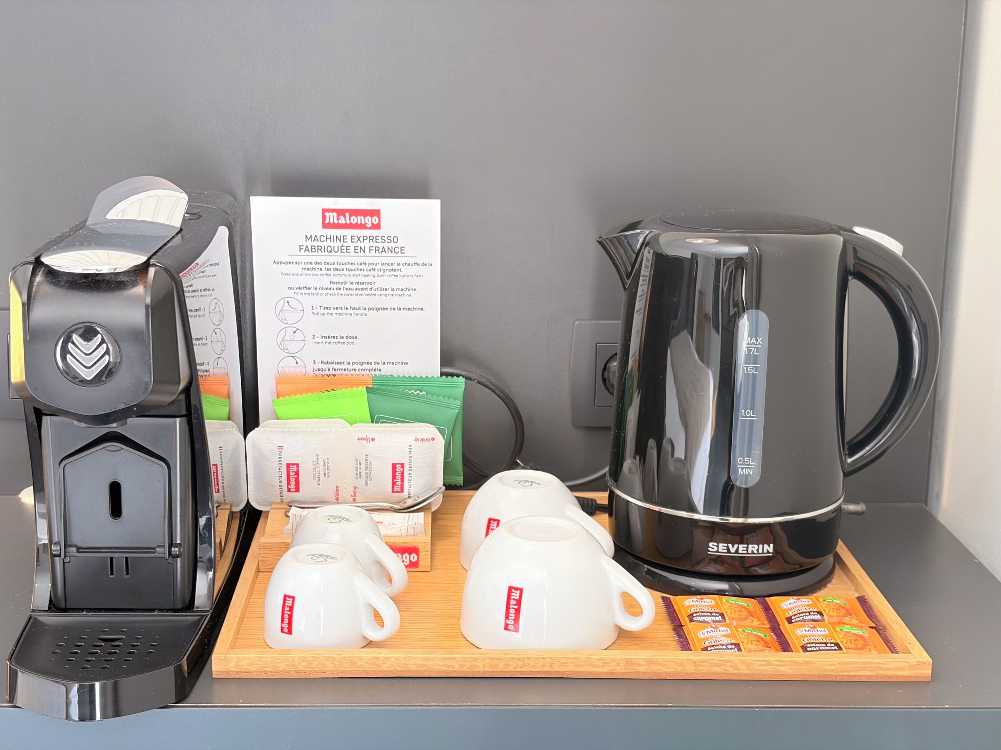 Une machine à café, une cafetière, des tasses et des dosettes de café, le tout posé sur un plateau en bois.