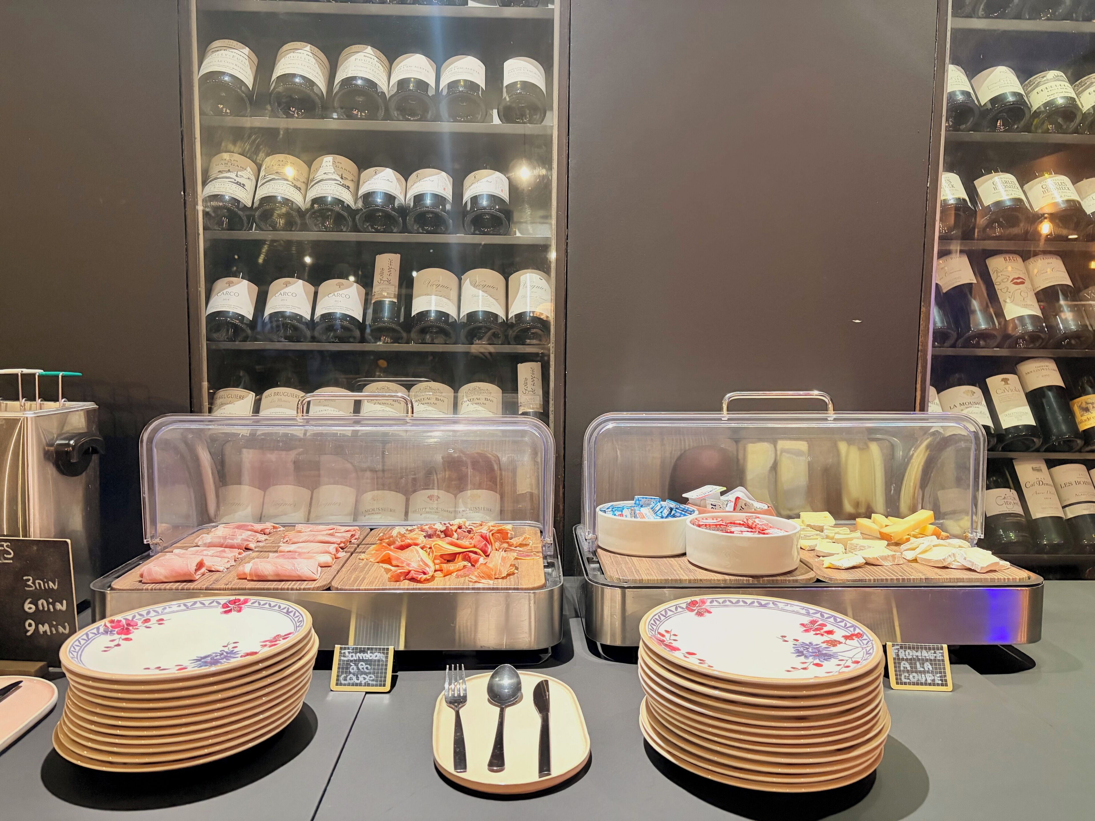 Ein Buffetbereich mit verschiedenen Speisen, darunter Fleisch- und Käseauswahl sowie eine Weinauswahl hinter Glasvitrinen.