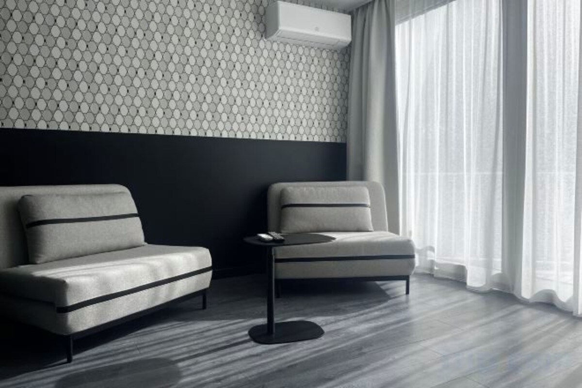 A modern room with two sofas and a small table, a patterned wall, and a window with curtains.