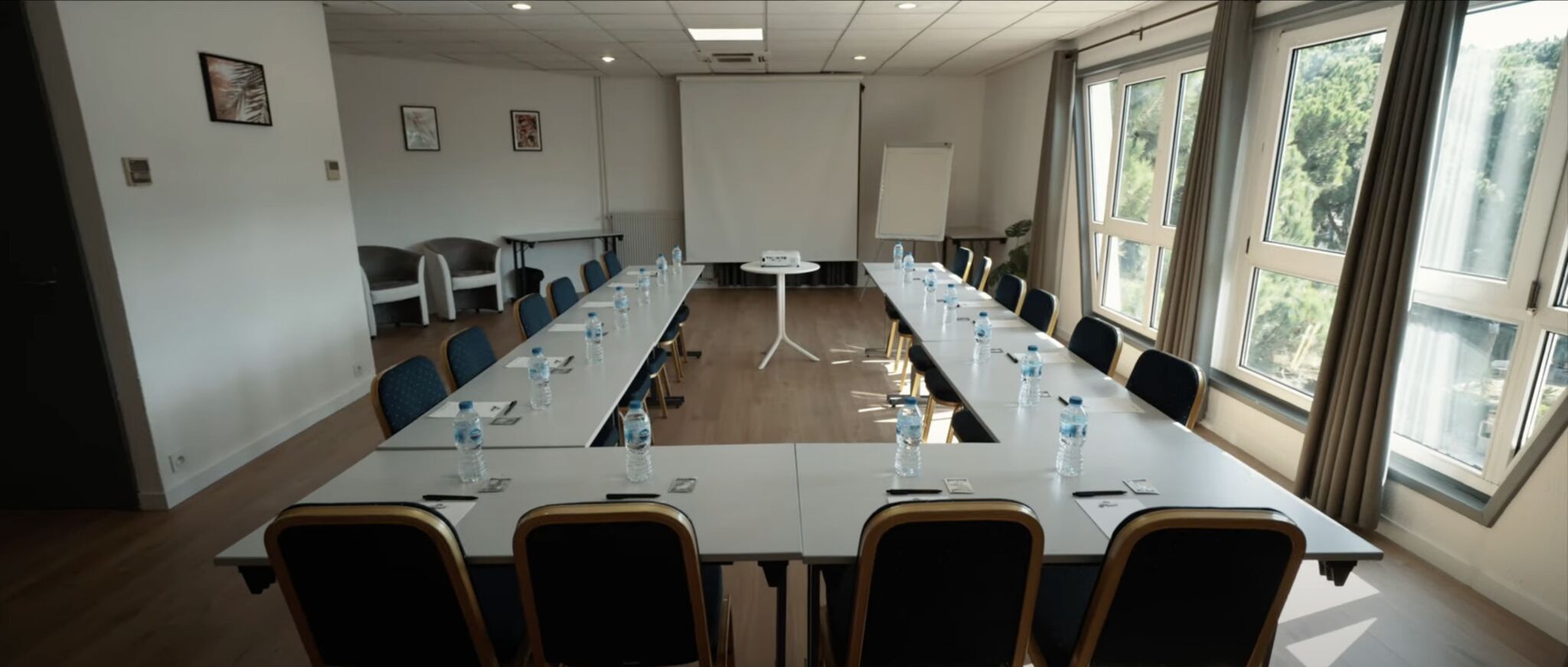 A conference room with a long table, chairs, water bottles, and a projector screen.