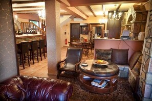 A cozy living area with leather furniture, a fireplace, and a bar area in the background. - Silva Suites (Lake Plastiras)
