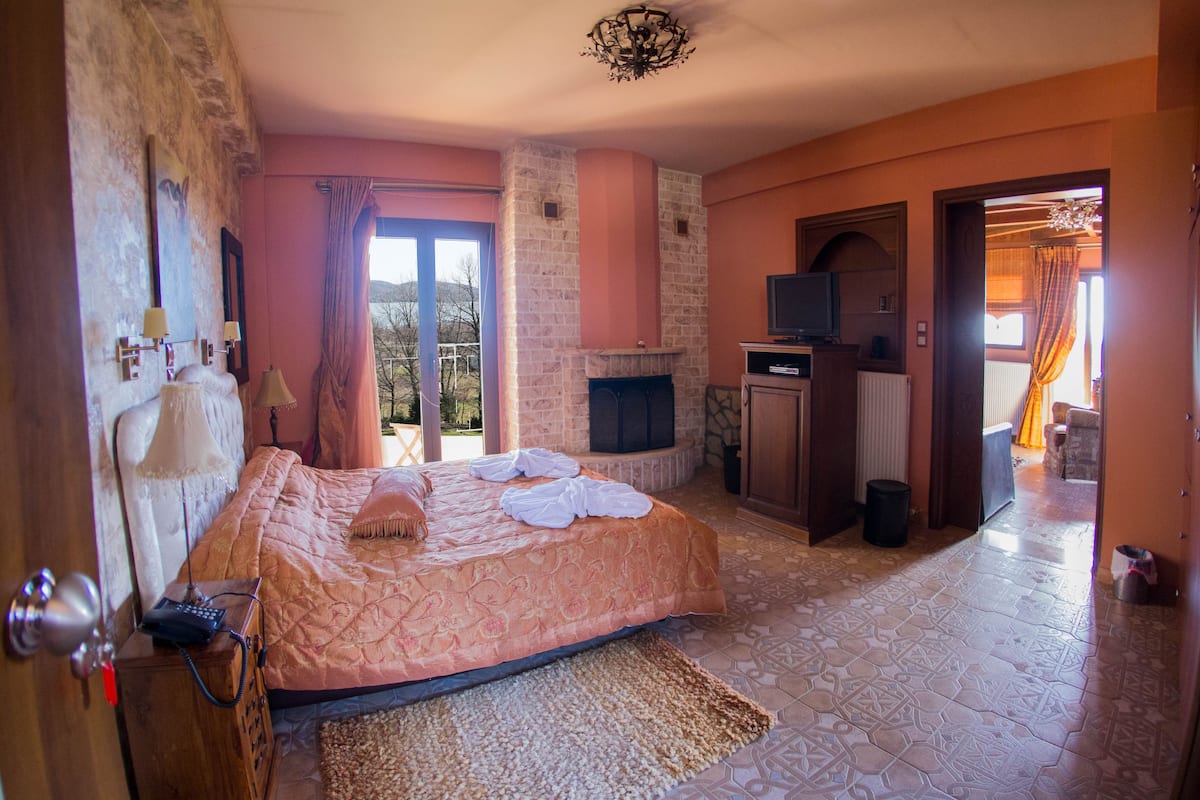 A bedroom with a bed, a fireplace, a television, and a view of the outdoors.