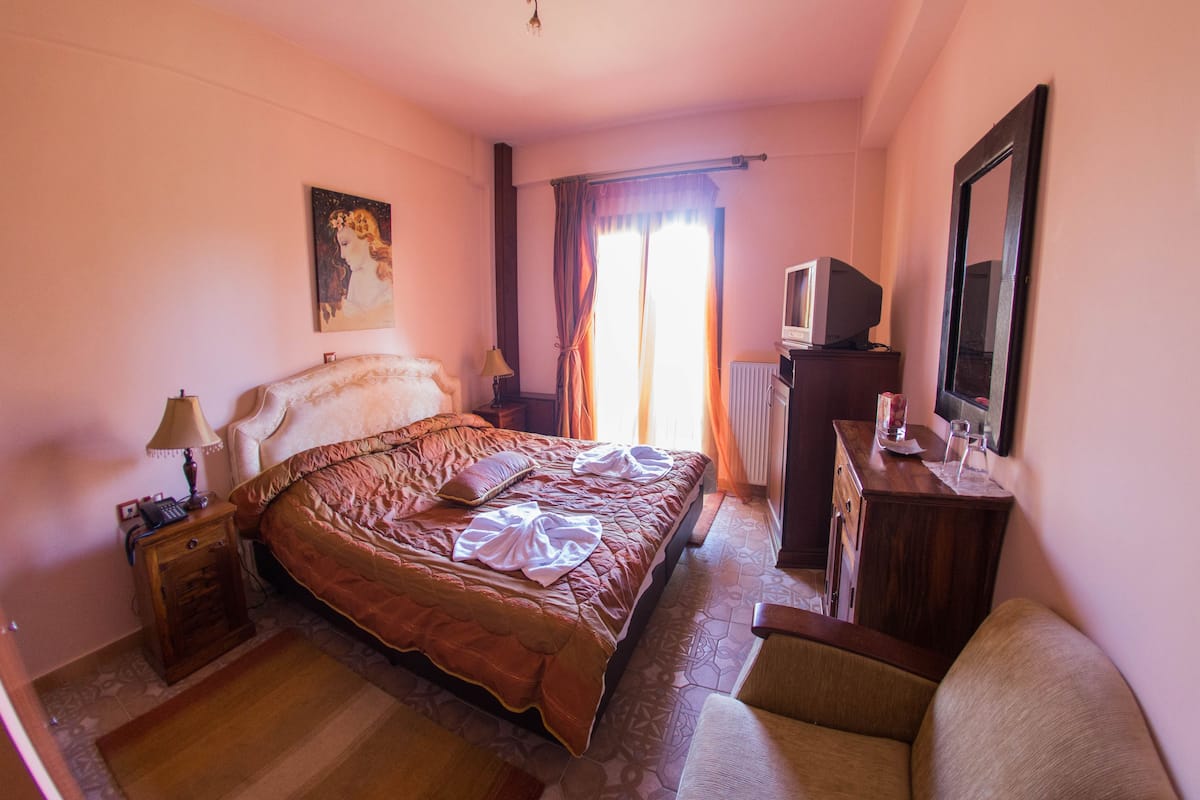 A hotel room with a bed, a desk with a mirror, a television, and a painting on the wall.