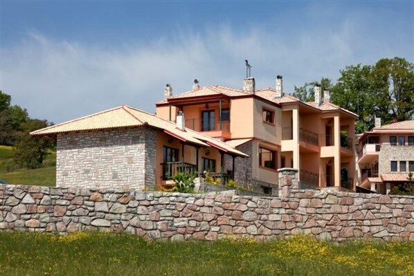 A two-story house with a stone facade, multiple chimneys, and a stone wall in front. - Silva Suites (Lake Plastiras)