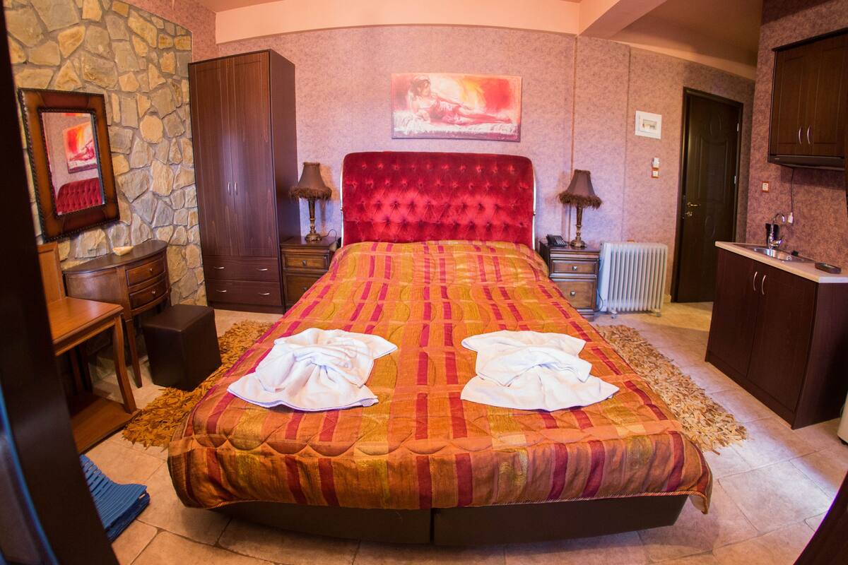 A bedroom with a large bed, a stone wall, a wooden wardrobe, a desk, and a painting on the wall.