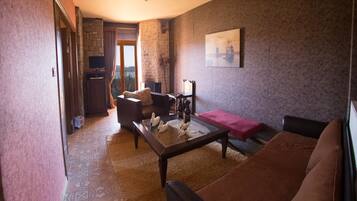 Una sala de estar con un sofá, una mesa de centro y una chimenea. Hay un cuadro en la pared y una ventana con vistas a árboles.