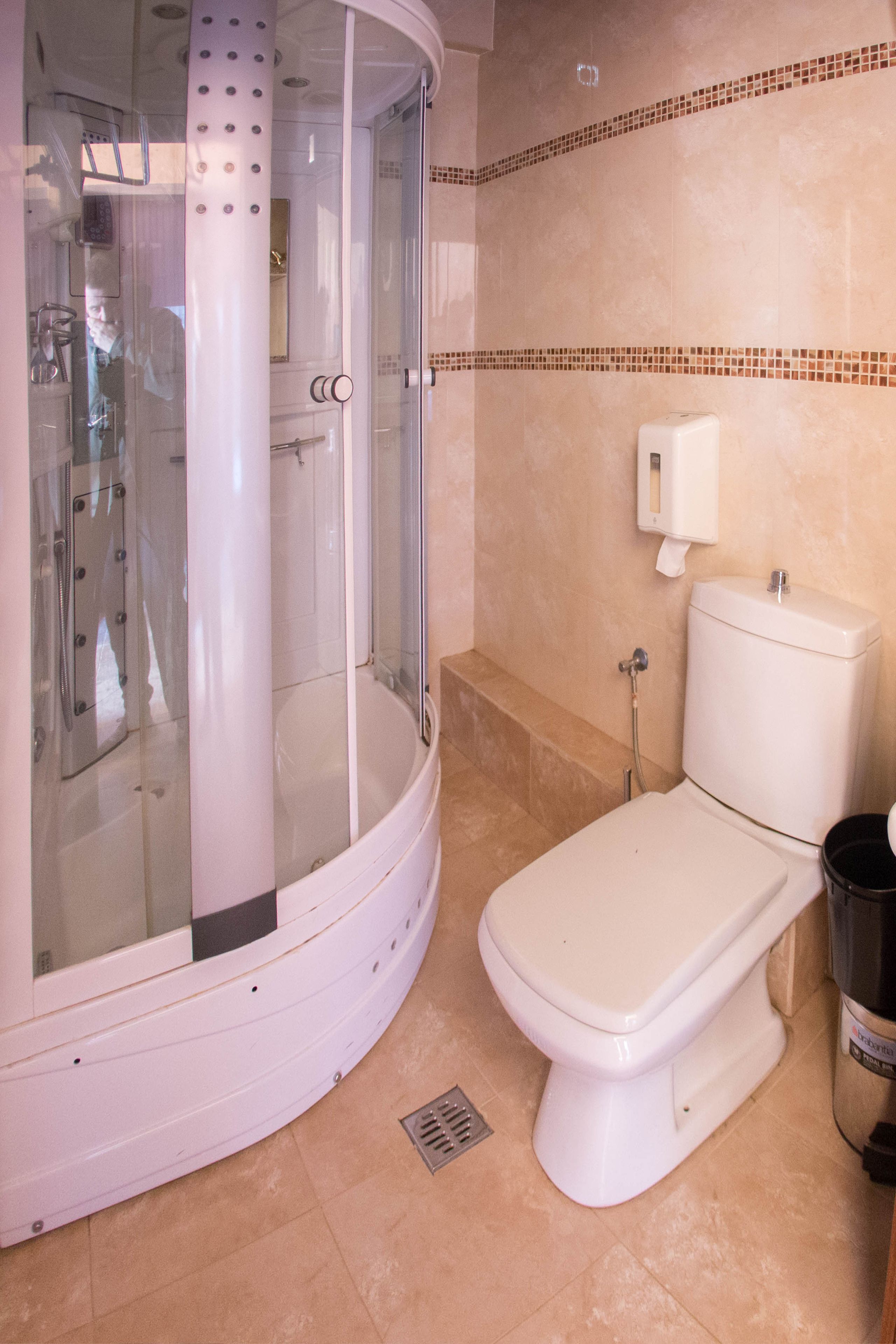 Un baño con ducha envuelta en vidrio, inodoro y cubo de basura.