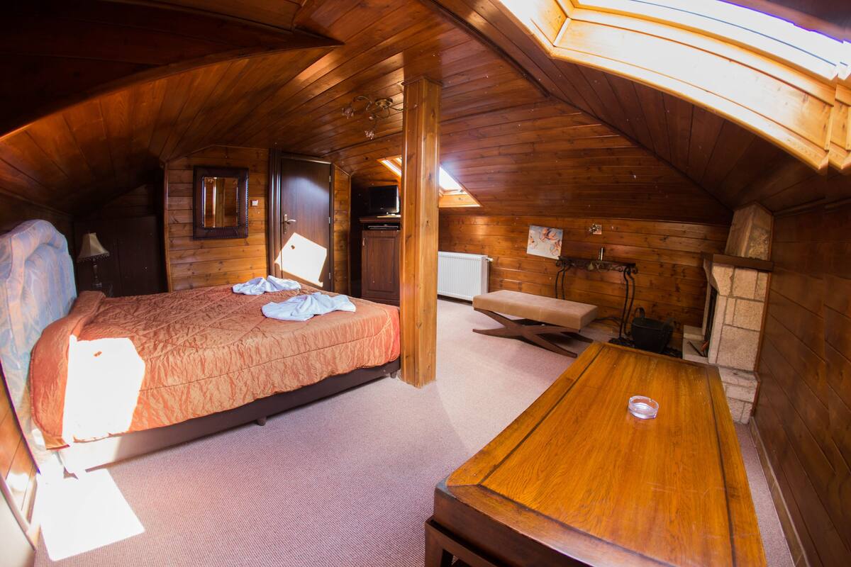 A cozy attic bedroom with a bed, a wooden table, and a small seating area.