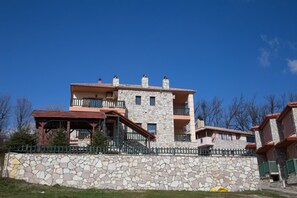 A multi-story stone building with balconies and a stone wall in front. - Silva Suites (Lake Plastiras)
