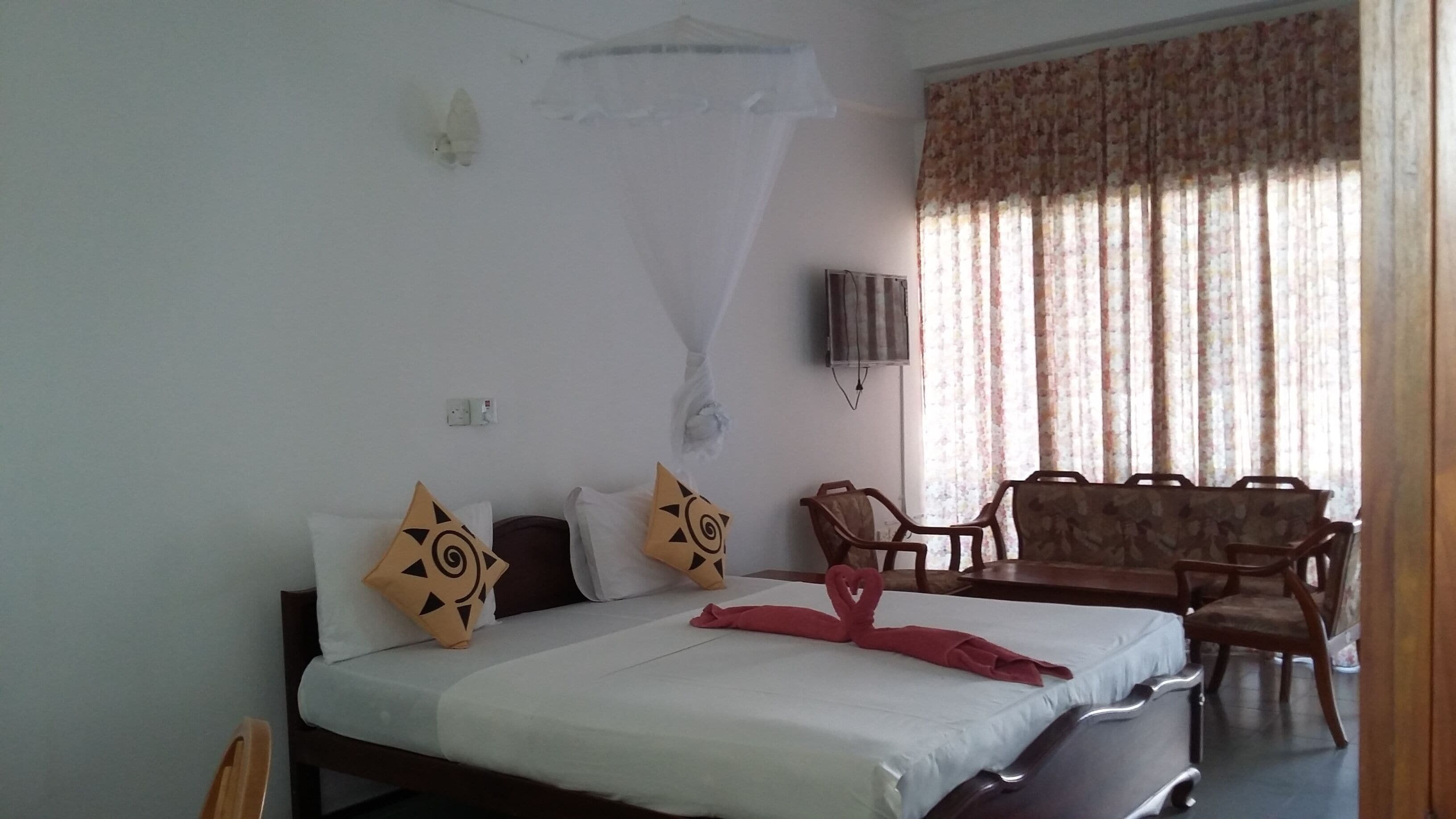 Una habitación de hotel con cama, una silla, una mesa y un mosquitero.