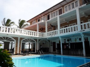 A multi-story building with a swimming pool, outdoor seating, and a covered patio area. - Oasis Beach Resort (Negombo)
