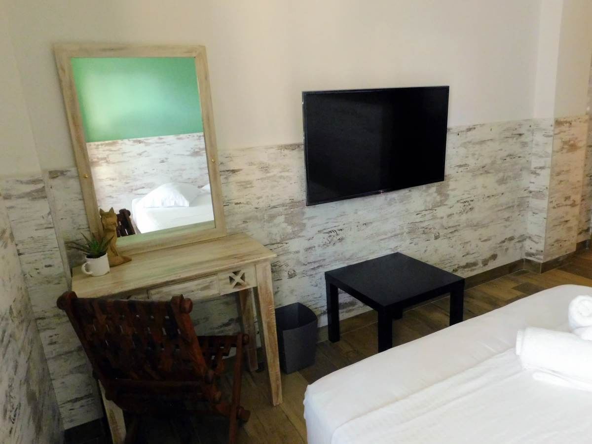 A room with a bed, a desk, a chair, a small table, a TV, and a trash bin.