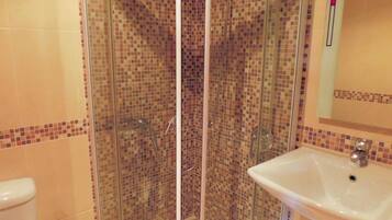 A bathroom with a glass-enclosed shower, a white sink, and tiled walls.