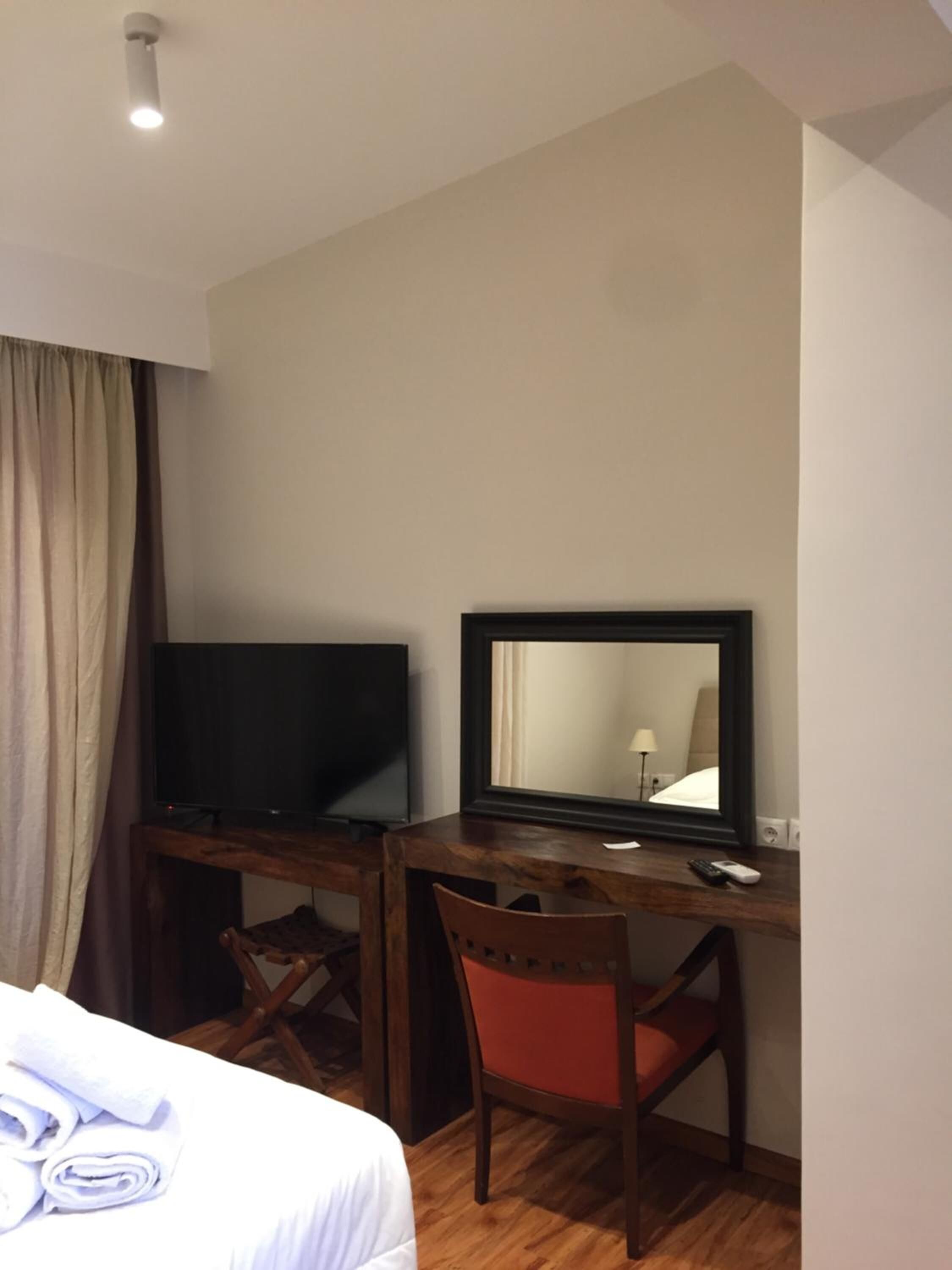 Una habitación de hotel con una cama, un escritorio con televisor, una silla y un espejo.