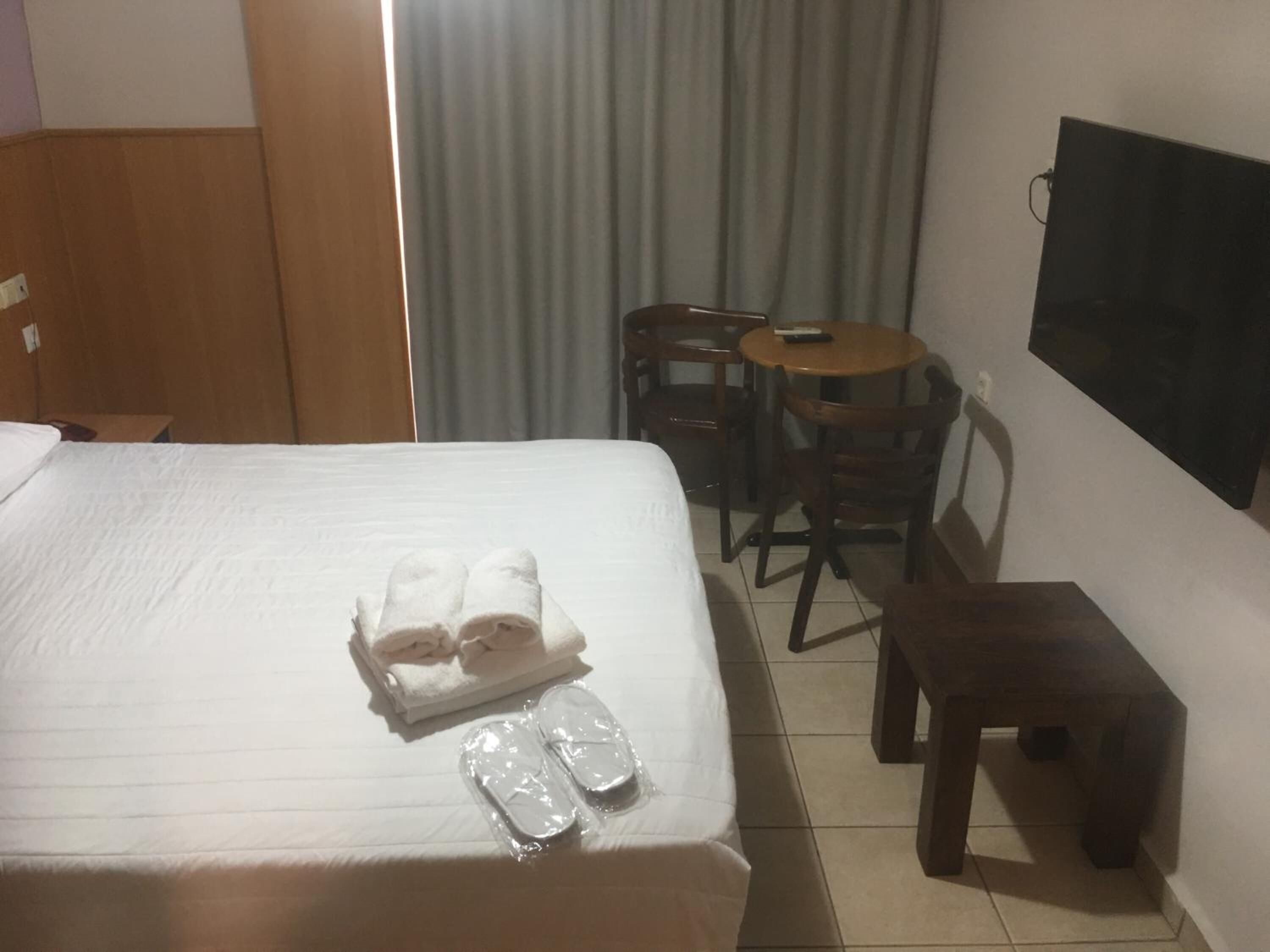 A hotel room with a bed, a small wooden table, two chairs, and a TV mounted on the wall.