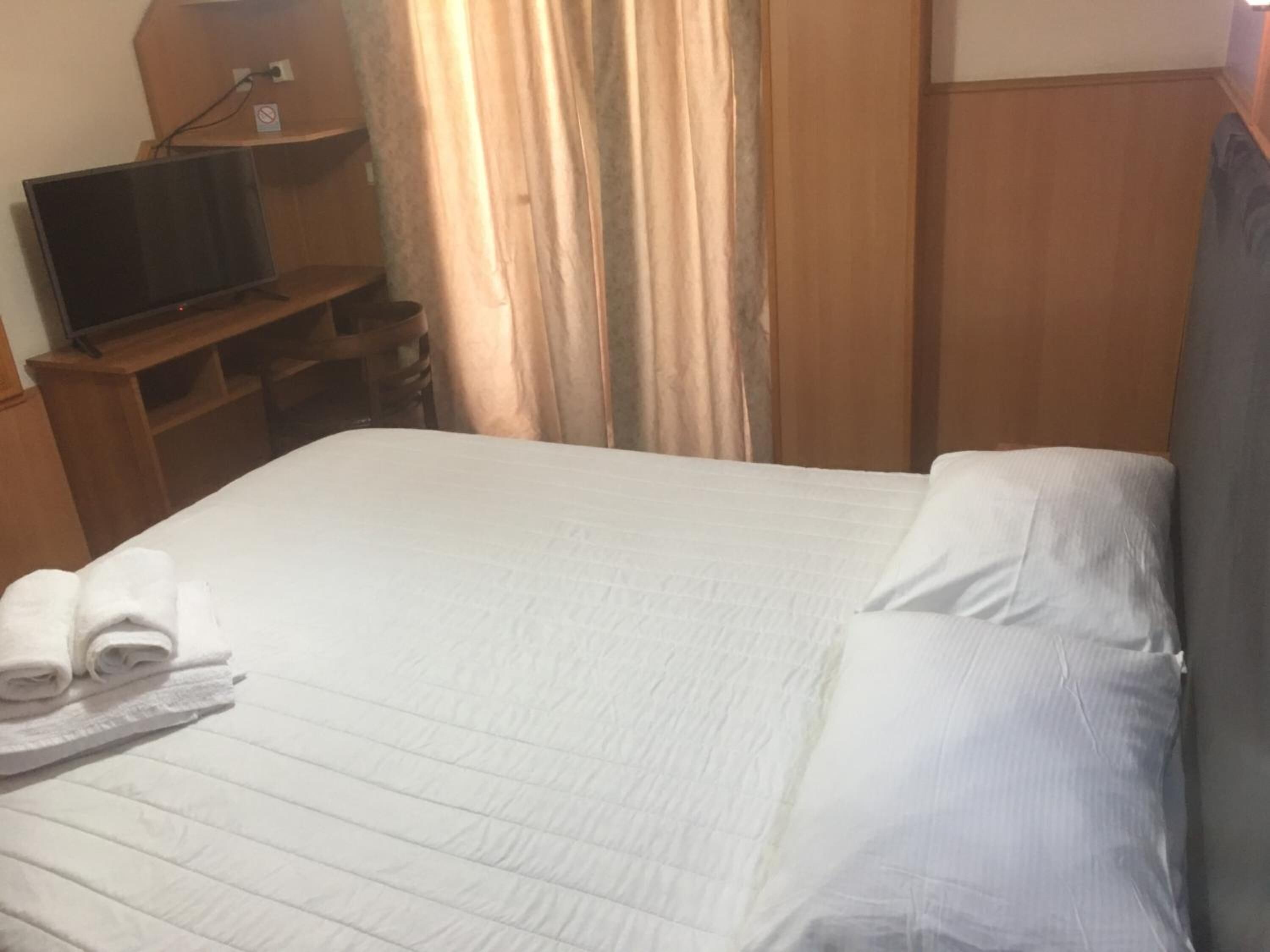 Una habitación de hotel con una cama, un televisor sobre un mueble de madera y una cortina.