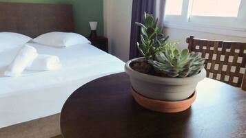 A neatly made bed with white linens and pillows, a potted succulent plant on a round table, and a wooden chair.
