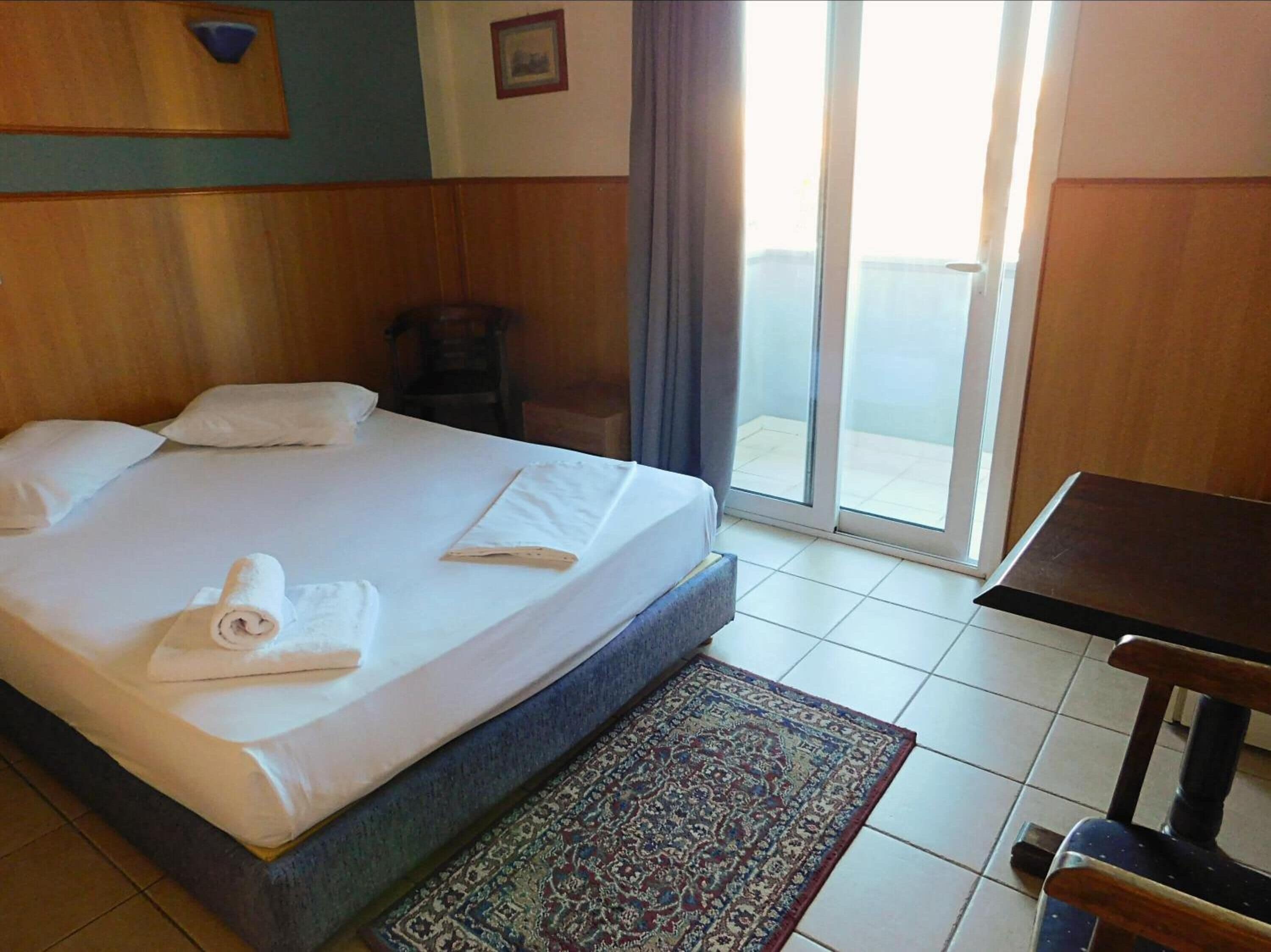 A hotel room with a bed, a chair, a table, and a view of the outside.