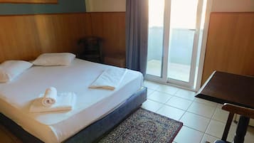 A hotel room with a bed, a chair, a table, and a view of the outside.