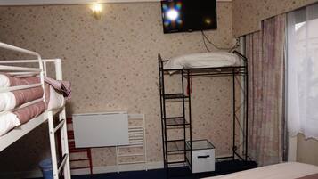 A room with bunk beds, a desk, a TV, and a window with curtains.