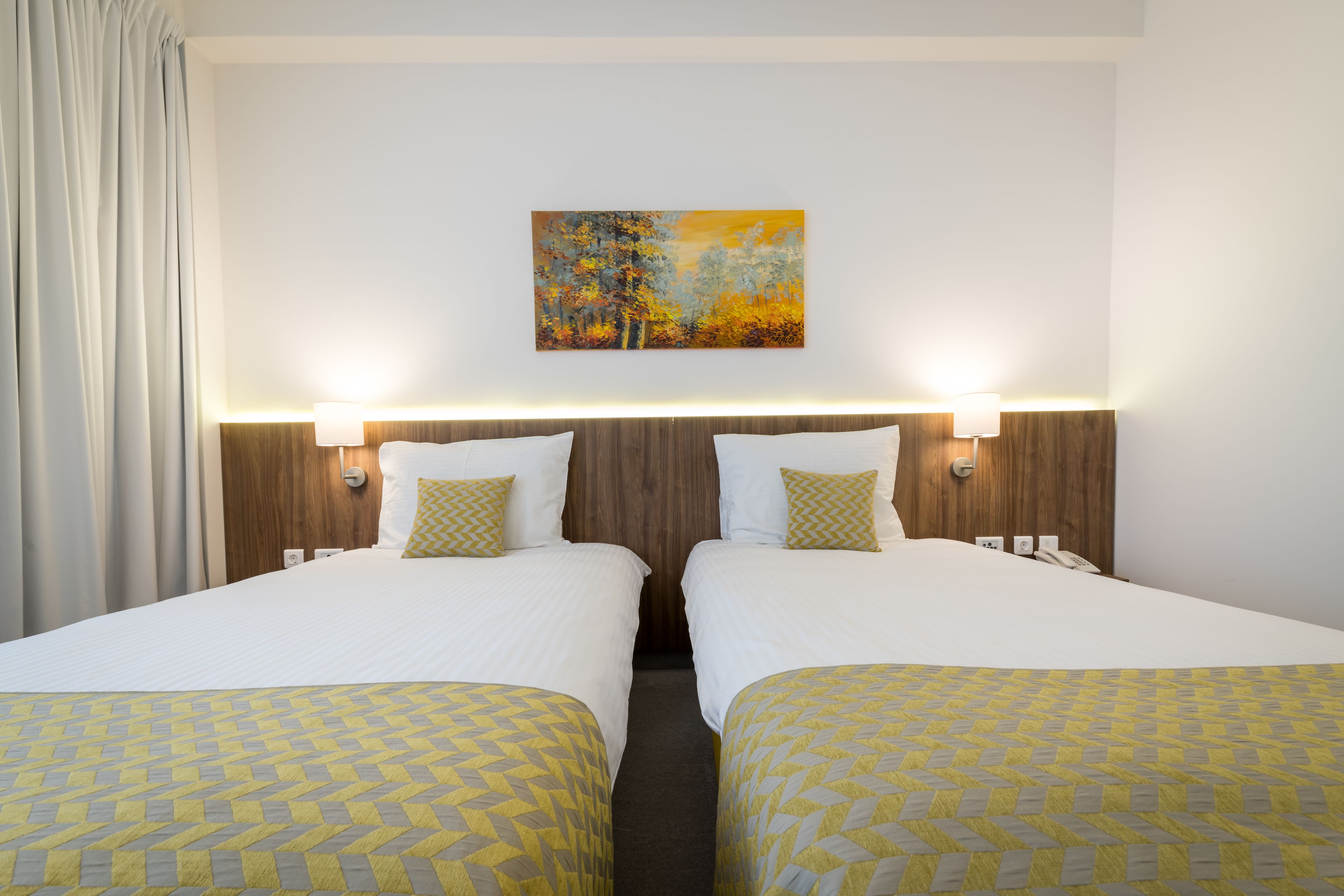 A hotel room with two beds, a painting on the wall, and bedside lamps.