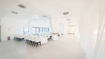 Een ruime, goed verlichte kamer met witte wanden en een hoge plafond, met een lange tafel gedekt voor een formeel evenement.