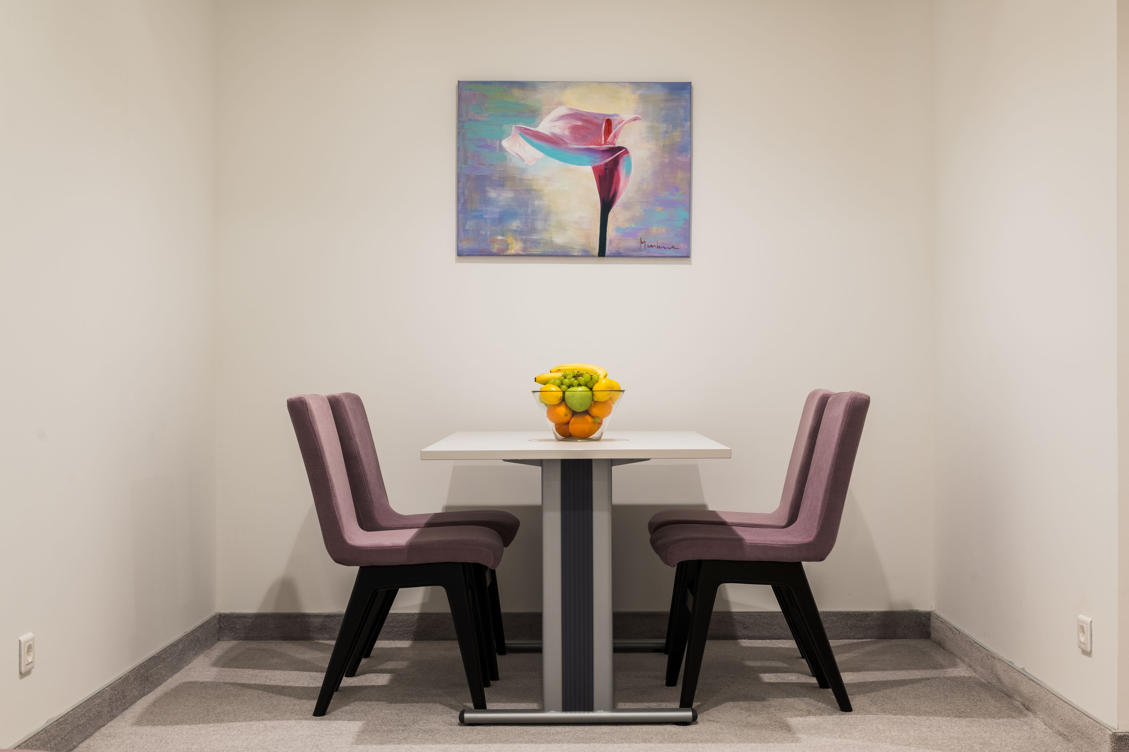 A dining area with a white table, purple chairs, and a fruit bowl on the table.