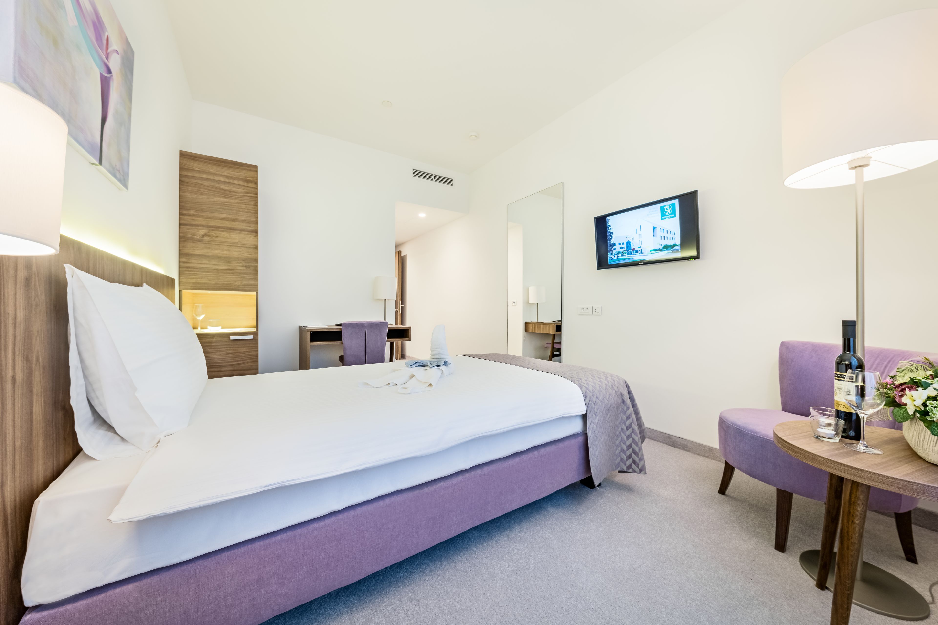 Een moderne hotelkamer met een groot bed, een bureau, een stoel, een televisie en een tafeltje met een fles en glazen.