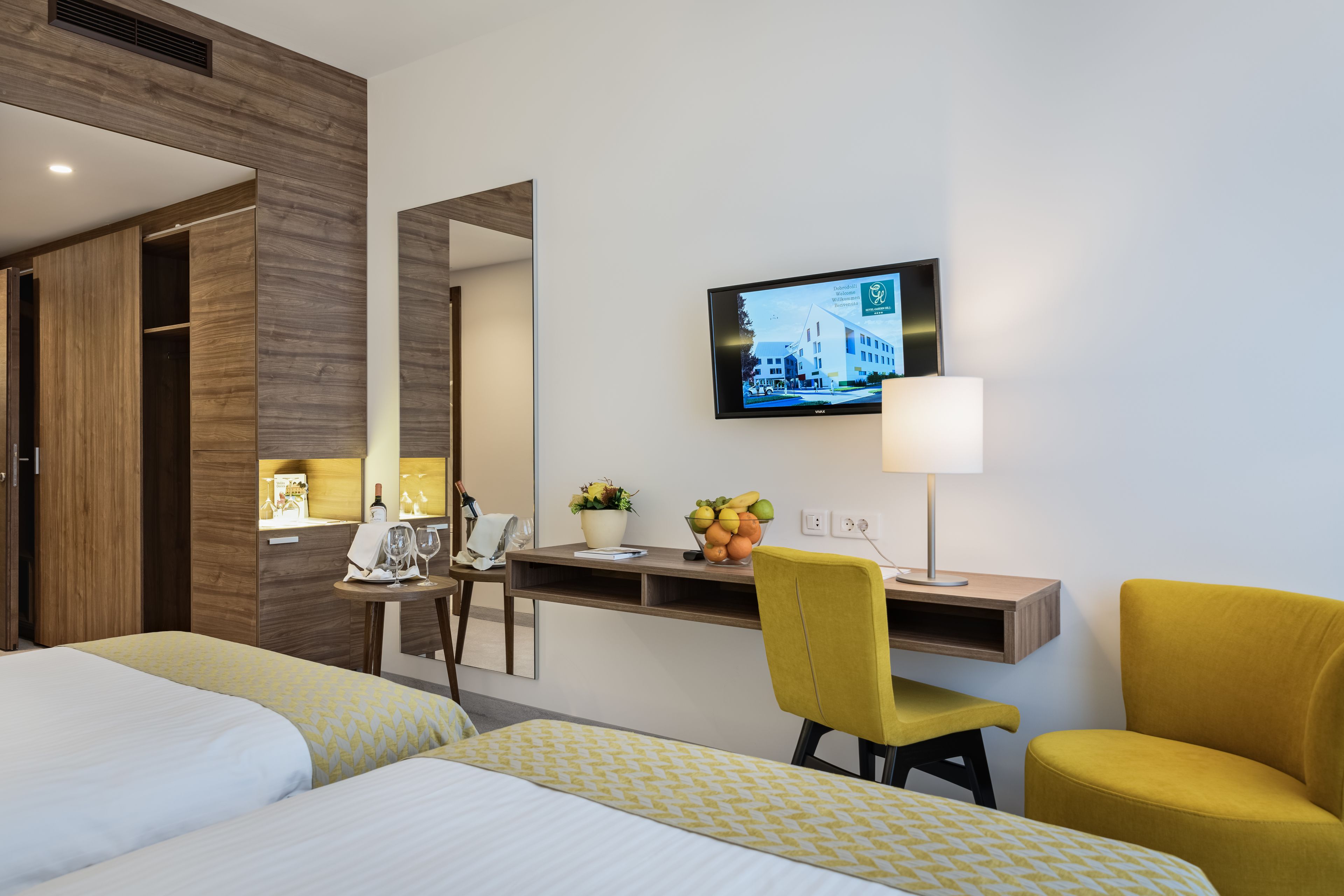 Habitación de hotel con dos camas, un escritorio con silla, televisor y lámpara.