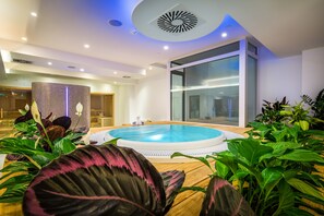 Un área de piscina interior moderna con un jacuzzi, rodeada de plantas exuberantes y un amplio ventanal.