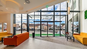 A hotel lobby with large windows, a reception desk, and yellow sofas.