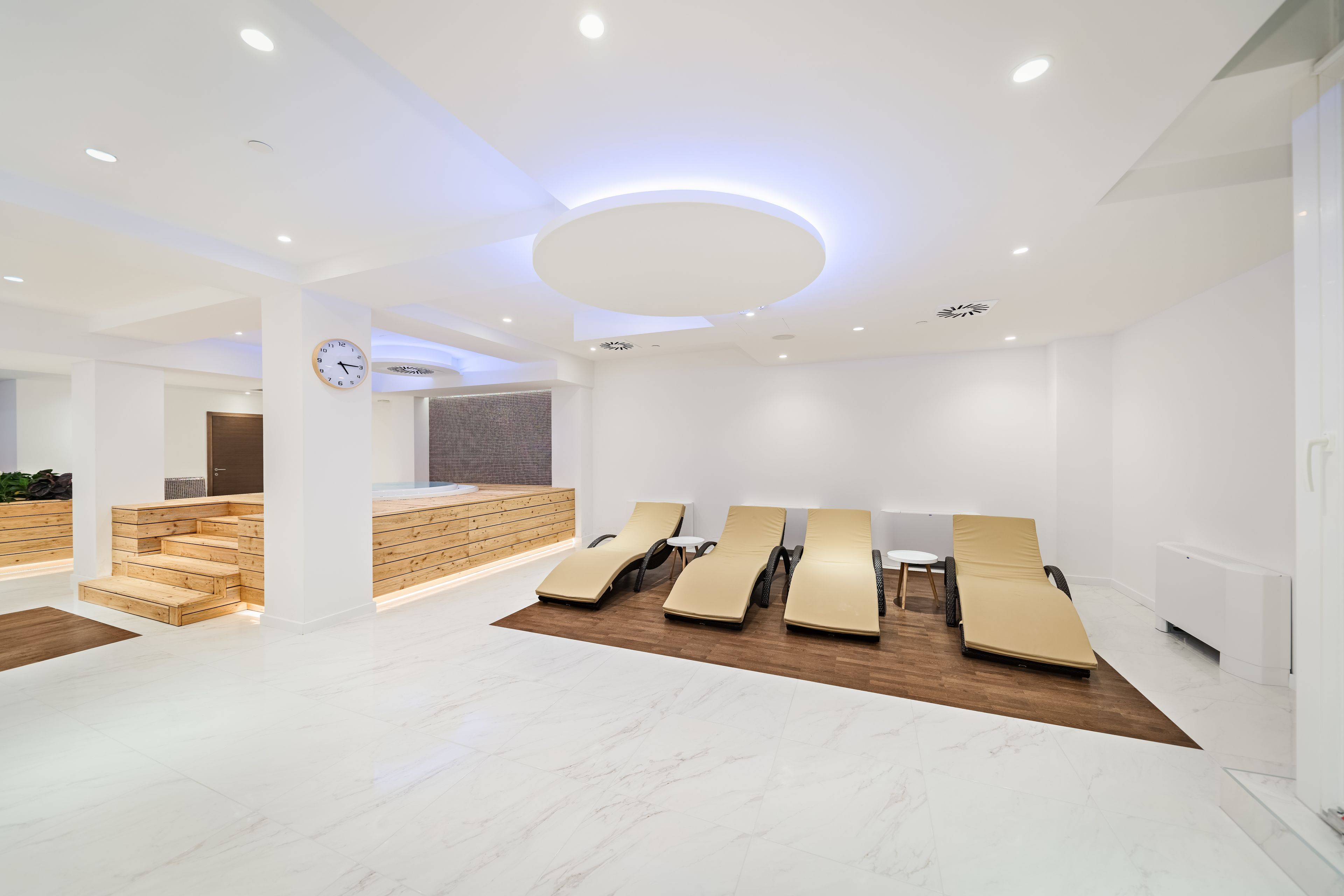 A modern spa room with a reception desk, wooden steps, and multiple sun loungers.