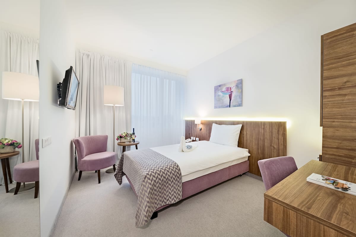 Ein Hotelzimmer mit Bett, Schreibtisch, zwei Stühlen, einem kleinen Tisch und einem an der Wand montierten Fernseher.