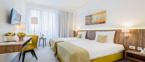 Habitación de hotel con dos camas, un escritorio con silla, televisión y un cuadro en la pared.