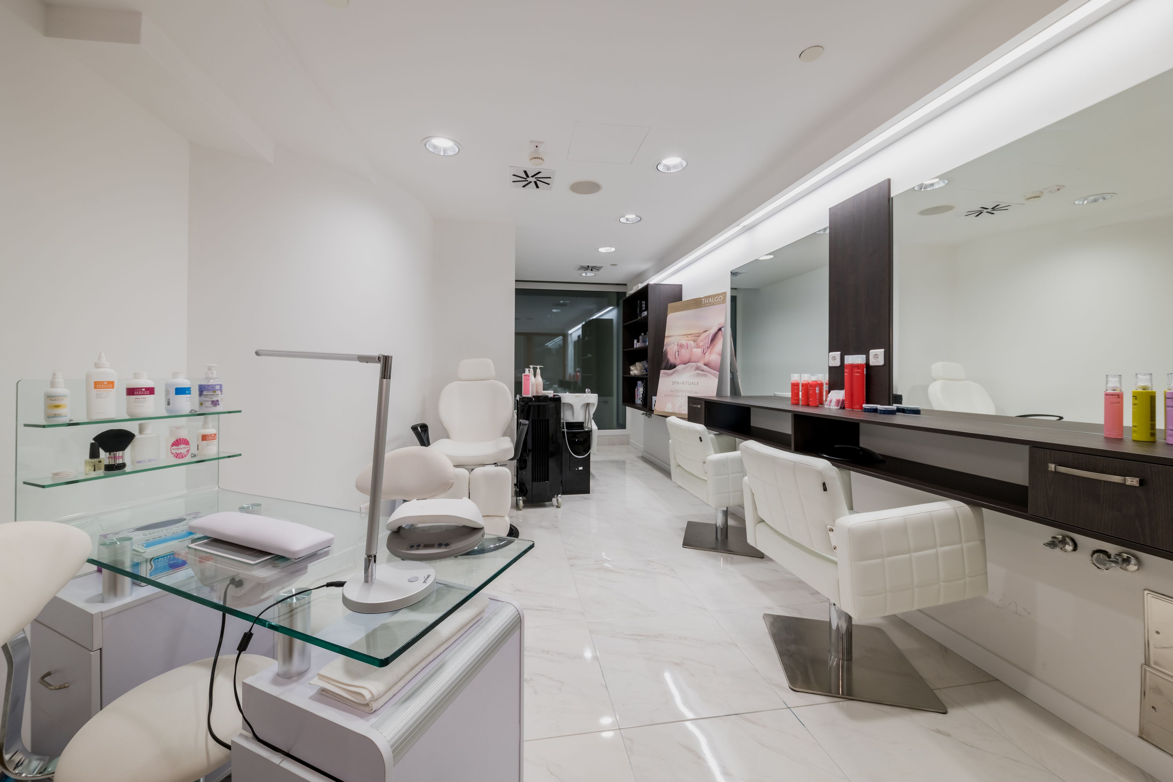 A modern, well-lit salon with white chairs, a glass counter, and a large mirror.