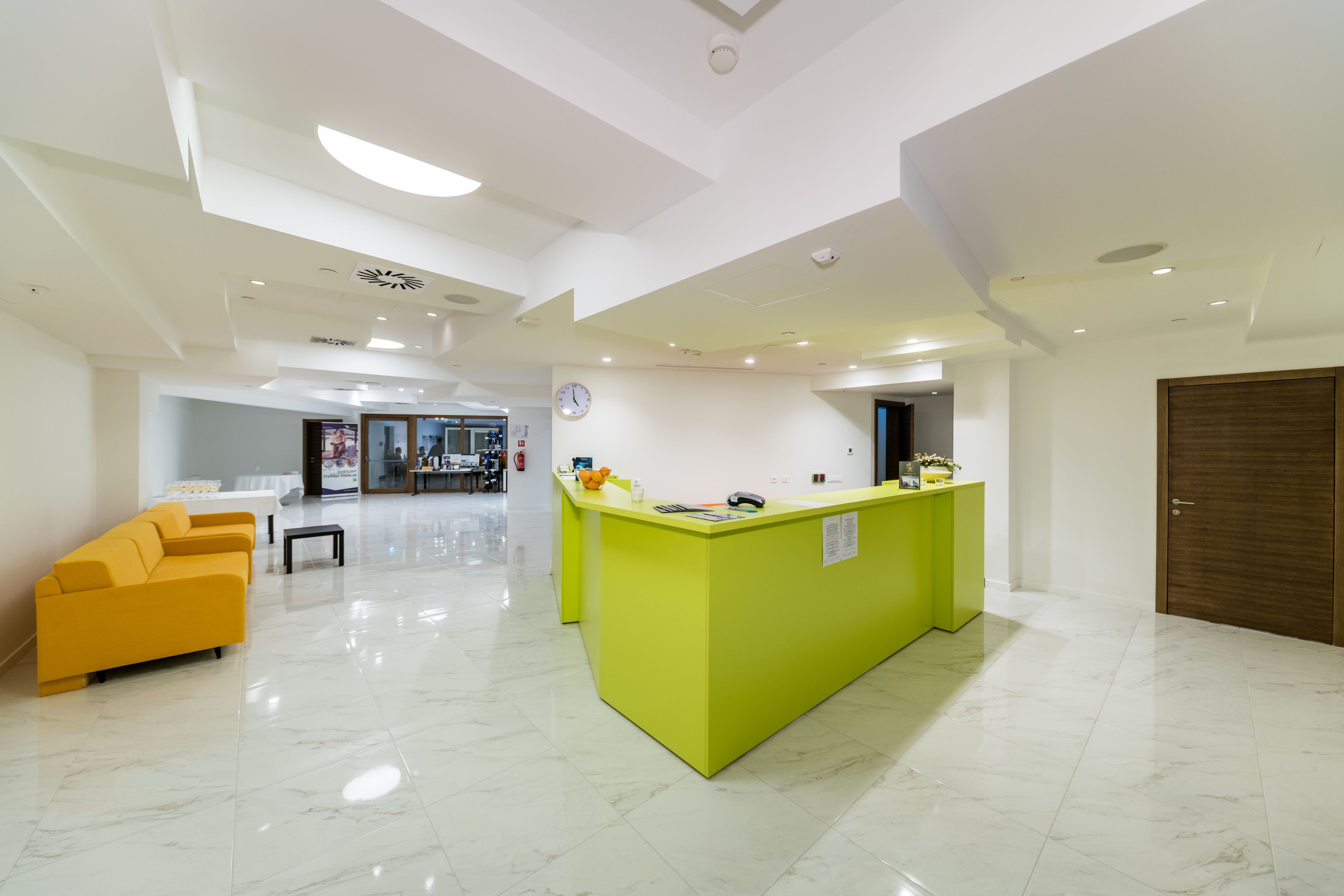 Un hall moderno con un mostrador de recepción amarillo brillante, un sofá amarillo y un suelo de mármol blanco.