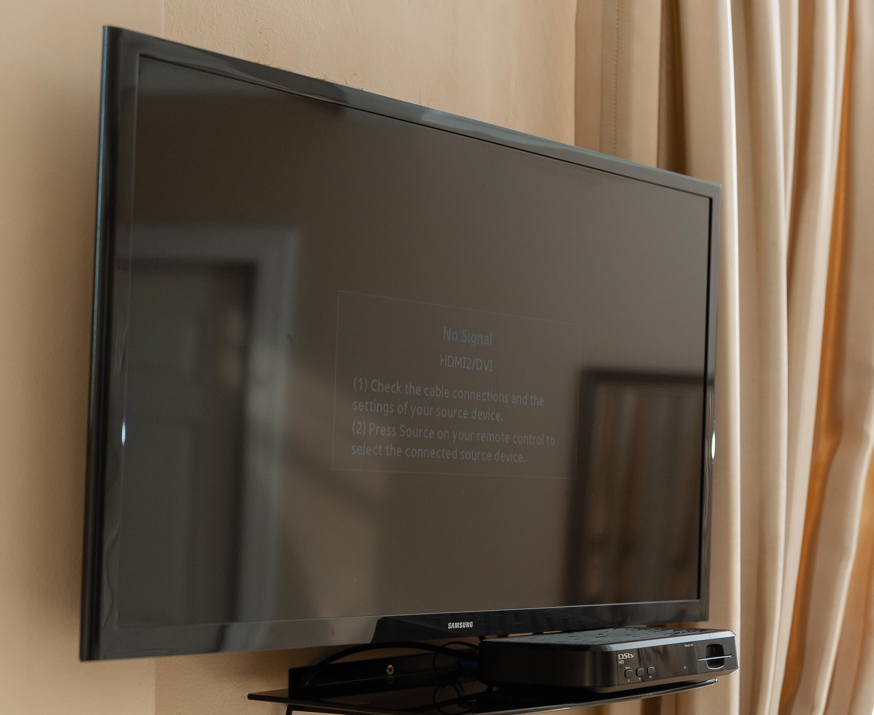 A flat-screen TV mounted on a wall with a DStv receiver below it.