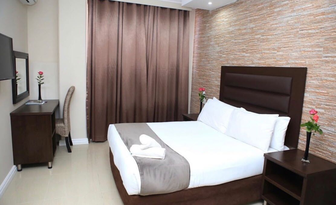 Une chambre d’hôtel avec un grand lit, une tête de lit en bois, un bureau avec une chaise et un rideau.