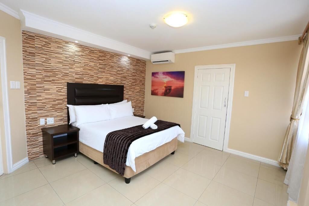 Habitación de hotel ordenada con cama, mesita de noche y aire acondicionado de pared.