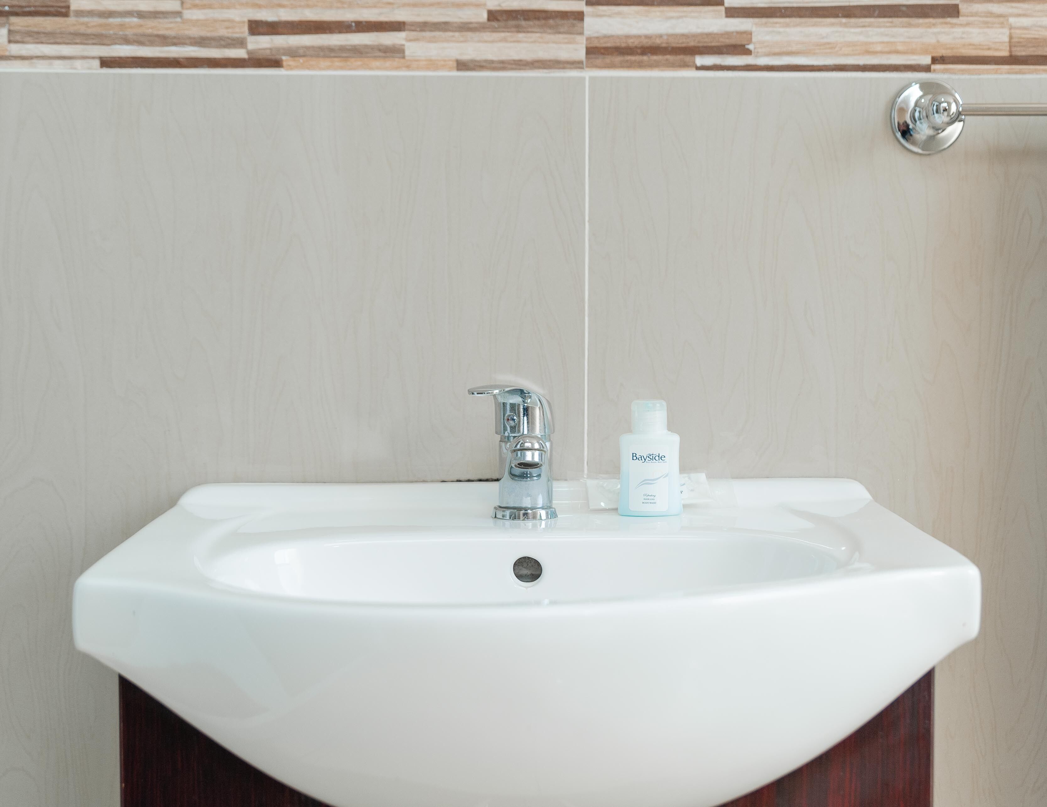 A white bathroom sink with a chrome faucet and a bottle of BaySide soap on the counter.